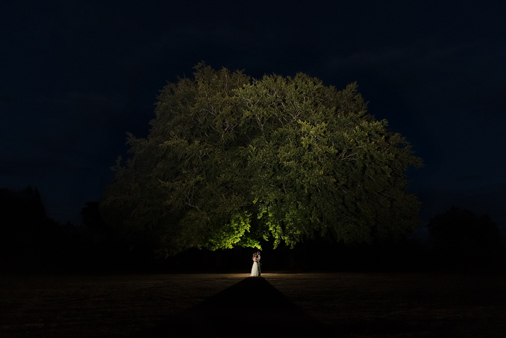 Dramatic night portrait of newlyweds under illuminated oak tree by Once in a Lifetime Photography Worcestershire